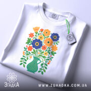 Футболка квіти Україна, біла футболка, складена на поверхні, з принтом букету квітів у вазі, яскраві кольори квітів, фон світло-сірий, на футболці є етикетка з зеленим шнурком.
