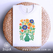 Футболка квіти Україна, біла футболка, розкладена на плетеній кошику, з принтом букету квітів у вазі, яскраві кольори, фон білий, ракурс зверху.