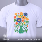 Футболка квіти Україна, біла футболка, складена на поверхні, з принтом букету квітів у вазі, яскраві кольори квітів, фон світло-сірий, на футболці є етикетка з зеленим шнурком.