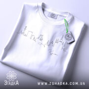 Футболка київський контур міста, біла, зображена в складеному вигляді, фон світло-сірий, принт у вигляді контурів міста виконаний чорним кольором, на футболці є етикетка з зеленим шнурком.