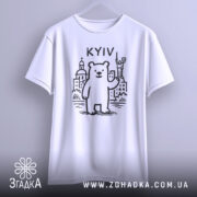 Футболка київський ведмідь, біла, підвішена на вішалці, фон світло-сірий, принт з ведмедем та архітектурними елементами Києва, напис 'KYIV' над ведмедем.