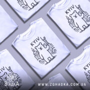 Футболка київський ведмідь, біла, зображена на манекені, фон світло-сірий, принт з ведмедем та архітектурними елементами Києва, напис 'KYIV' над ведмедем.