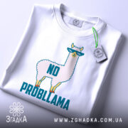 Футболка лама білого кольору, складена на столі, фон світло-сірий, принт з ламою в окулярах та написом 'NO PROBLLAMA', на футболці є етикетка з зеленим шнурком.