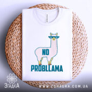 Футболка лама білого кольору, складена на плетеному кошику, фон світло-сірий, принт з ламою в окулярах та написом 'NO PROBLLAMA', видно етикетку з написом.