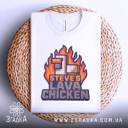 Футболка лава курка Майкрафт, біла, лежить на круглій кошику, фон світло-сірий, принт з вогняними елементами та текстом 'STEVE'S LAVA CHICKEN' у фіолетових та помаранчевих кольорах.