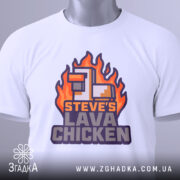 Футболка лава курка Майкрафт, біла, лежить на столі, фон світло-сірий, принт з вогняними елементами та текстом 'STEVE'S LAVA CHICKEN' у фіолетових та помаранчевих кольорах, з етикеткою на зеленому шнурку.