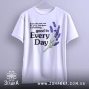 Футболка лаванда гарний настрій. Біла футболка на вішалці, з принтом, що містить текст і зображення лаванди. Принт розташований по центру, текст чорного кольору, а лаванда виконана в фіолетових відтінках. Фон світло-сірий, що підкреслює яскравість кольорів.