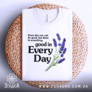 Футболка лаванда гарний настрій. Біла футболка, складена на плетеній кошику, з принтом, що містить текст і зображення лаванди. Принт розташований по центру, текст чорного кольору, а лаванда виконана в фіолетових відтінках. Фон натурального кольору плетеного кошика, що додає текстури.