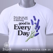 Футболка лаванда гарний настрій. Біла футболка, складена на поверхні, з принтом, що містить текст і зображення лаванди. Принт розташований по центру, текст чорного кольору, а лаванда виконана в фіолетових відтінках. На футболці є етикетка з зеленим шнурком, фон світло-сірий.