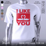 Футболка лебеді кохання, біла, зображена з фронтального ракурсу, на фоні світло-сірого градієнту, принт червоного кольору з написом 'I LIKE YOU' та двома лебедями, що з'єднують свої голови.