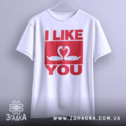 Футболка лебеді кохання, біла, підвішена на вішалці, фон світло-сірий, принт червоного кольору з написом 'I LIKE YOU' та двома лебедями, що з'єднують свої голови.
