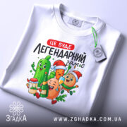 Футболка легендарний заміс, біла, зображена зверху, фон світлий, принт з веселими овочами та фруктами, на футболці є етикетка.