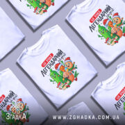 Футболка легендарний заміс, біла, зображена на манекені, фон градієнтний сірий, принт з веселими овочами та фруктами в святкових шапках.