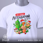 Футболка легендарний заміс, біла, зображена зверху, фон світлий, принт з веселими овочами та фруктами, на футболці є етикетка.