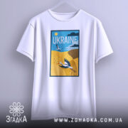 Футболка лелеки летять, біла, підвішена на вішалці, фон світло-сірий, принт з лелекою на жовтому полі та написом 'UKRAINE' у верхній частині.
