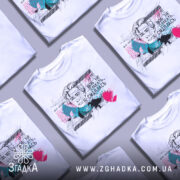 Футболка Леся емоції. Біла футболка, складена в кілька шарів, з принтом, що зображує жінку з коротким волоссям. На фоні кольорові плями та текст українською мовою.