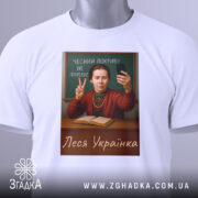 Футболка Леся Українка білого кольору, зображена на столі, принт з портретом жінки, яка тримає телефон, на фоні дошки, з написом 'Чесний покрив не потрібен', на футболці є етикетка з зеленим шнурком.