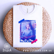 Футболка Леся Українка білого кольору, зображена зверху на плетеній кошику, фон світло-сірий, принт з Лесею Українкою, кольорові елементи на принті, текст написаний українською.