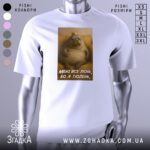 Футболка лєнь я тюлень, біла футболка з принтом, зображення тюленя з короною на фоні жовтого дивану, текст на футболці: 'МЕНІ ВСЕ ЛЄНЬ, БО Я ТЮЛЕНЬ'.