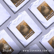 Футболка лєнь я тюлень, біла футболка з принтом, зображення тюленя з короною на фоні жовтого дивану, текст на футболці: 'МЕНІ ВСЕ ЛЄНЬ, БО Я ТЮЛЕНЬ'.