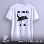 Футболка лінивий кіт, білого кольору, підвішена на вішалці, фон світло-сірий, принт чорного кота, що лежить на логотипі, з текстом 'JUST DO IT. LATER.' у чорному кольорі.