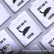 Футболка лінивий кіт, білого кольору, зображена з близького ракурсу на манекені, фон світло-сірий, принт чорного кота, що лежить на логотипі, з текстом 'JUST DO IT. LATER.' у чорному кольорі.