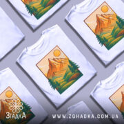 Футболка ліс і гори, біла, зображена з фронтального ракурсу, фон нейтральний, принт з горами, сонцем та деревами в зелених і жовтих тонах.