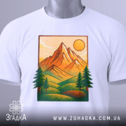 Футболка ліс і гори, біла, зображена зверху, фон світлий, принт з горами, сонцем та деревами, з етикеткою на шнурку.