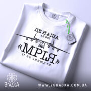 Футболка літак мрія, біла, складена на столі, з видимим етикеткою, фон світлий, принт з літаком АН-225 та написом «МРІЯ» чорного кольору.