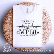 Футболка літак мрія, біла, складена на плетеній основі, фон світлий, принт з літаком АН-225 та написом «МРІЯ» чорного кольору.