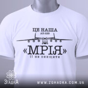 Футболка літак мрія, біла, складена на столі, з видимим етикеткою, фон світлий, принт з літаком АН-225 та написом «МРІЯ» чорного кольору.