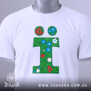 Футболка літера ї, біла, зображена зверху, фон світлий, принт у вигляді зеленого листя з червоними та синіми квітами, на футболці є етикетка.