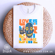 Футболка любов мова, біла, зображена зверху на плетеній основі, фон білий, принт з написом 'LOVE IS OUR LANGUAGE' у яскравих кольорах, з малюнком маски, що показує жест 'I love you'.