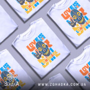 Футболка любов мова, біла, зображена з фронтального ракурсу, фон світло-сірий, принт з написом 'LOVE IS OUR LANGUAGE' у яскравих кольорах, з малюнком маски, що показує жест 'I love you'.