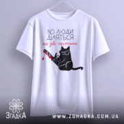 Футболка люди діляться: біла футболка на вішалці, з принтом чорного кота у окулярах, що тримає бензопилу з червоною плямою, фон світло-сірий.