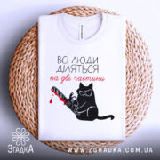 Футболка люди діляться: складена біла футболка з принтом чорного кота у окулярах, що тримає бензопилу з червоною плямою, на плетеній основі, фон світло-сірий.
