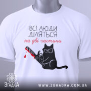 Футболка люди діляться: складена біла футболка з принтом чорного кота у окулярах, що тримає бензопилу з червоною плямою, на фоні світло-сірого кольору, з етикеткою зеленого кольору.