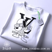 Футболка louis vuitton білого кольору, складена на поверхні, з видимим етикеткою, фон світло-сірий, принт з персонажем у вбранні з логотипом LV, що виконує жест.