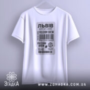 Футболка Львів місто історії, біла футболка з коротким рукавом, підвішена на вішалці, фон світлий, принт у вигляді етикетки з текстом 'FREEDOM BREW' та штрих-кодом.