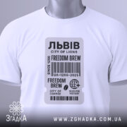 Футболка Львів місто історії, біла футболка, складена на столі, фон світлий, принт у вигляді етикетки з текстом 'FREEDOM BREW', прикріплений ярлик зеленого кольору.