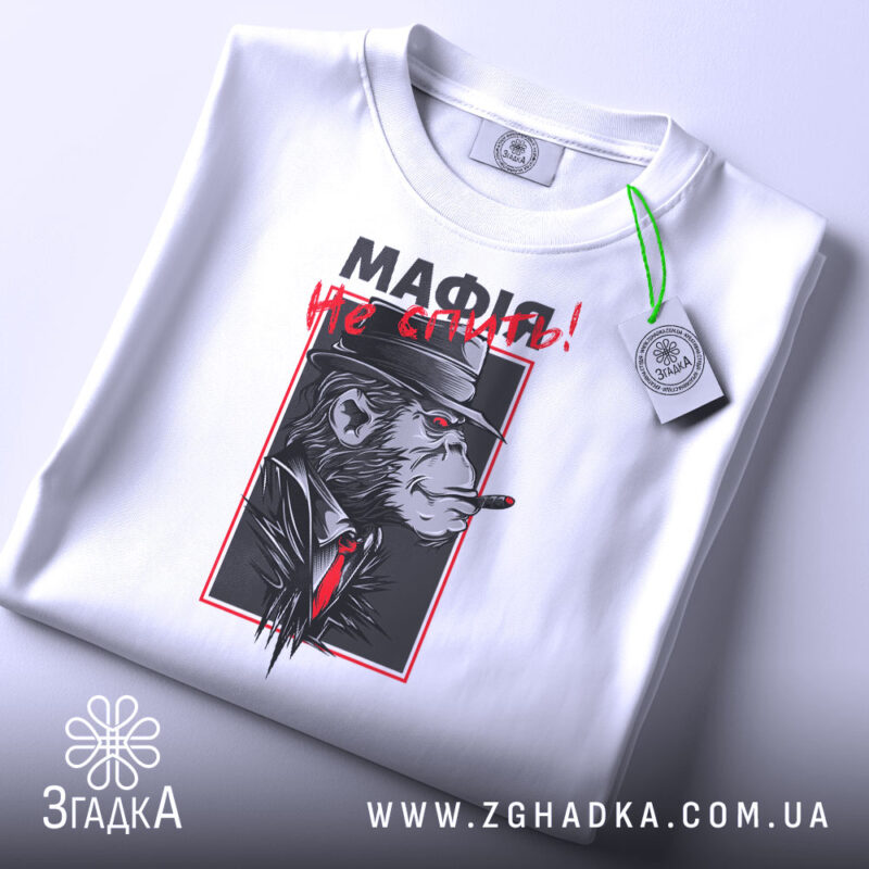 Футболка мафія не спить, складена біла футболка з принтом, зображення горили в капелюсі з сигарою, червоний текст "МАФІЯ не спить!", фон світло-сірий, ракурс зверху.