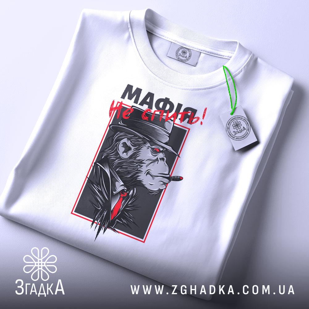 Футболка мафія не спить, складена біла футболка з принтом, зображення горили в капелюсі з сигарою, червоний текст "МАФІЯ не спить!", фон світло-сірий, ракурс зверху.