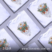 Футболка магія метелика білого кольору, зображена з фронтального ракурсу на манекені, фон світло-сірий, принт з метеликом в яскравих кольорах, оточений декоративними елементами.