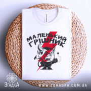 Футболка маленький грішник, біла, складена на плетеній кошику, фон світло-сірий, принт з червоним і чорним малюнком маленького диявола та написом.