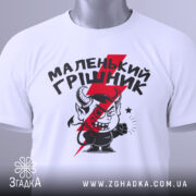 Футболка маленький грішник, біла, складена на поверхні, фон світло-сірий, принт з червоним і чорним малюнком маленького диявола та написом, з зеленим ярликом.