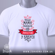 Футболка мама сказала ні. Біла футболка, складена на столі, з видимим принтом. Зображена з верхнього ракурсу. На фоні білий колір. Принт червоного та чорного кольорів з текстом та короною, з біркою на комірці.