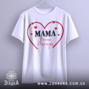 Футболка мама вічно молода, білого кольору, підвішена на вішалці, фон світло-сірий, принт у вигляді червоного серця з написом 'MAMA' чорним шрифтом та 'Вічно Молода' червоним шрифтом.