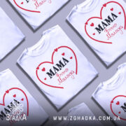 Футболка мама вічно молода, білого кольору, зображена на манекені в анфас, фон світло-сірий, принт у вигляді червоного серця з написом 'MAMA' чорним шрифтом та 'Вічно Молода' червоним шрифтом.