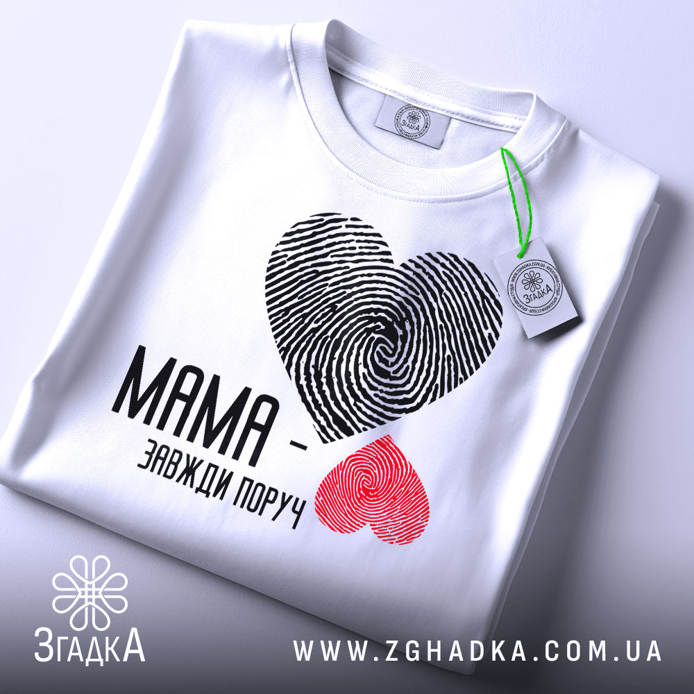 Футболка мама завжди поруч, білого кольору, складена на поверхні, фон світло-сірий, принт з сердець з відбитками пальців: чорне та червоне, текст чорного кольору, на комірці видна етикетка.