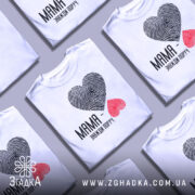 Футболка мама завжди поруч, білого кольору, зображена на манекені, фон світло-сірий, принт у вигляді сердець з відбитками пальців: чорне та червоне, текст чорного кольору під принтом.